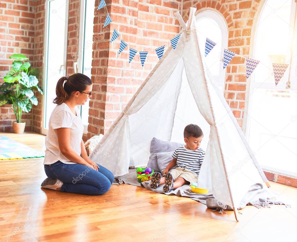 Beautiful teacher and toddler boy sitting on the floor playing inside  tipi at kindergarten