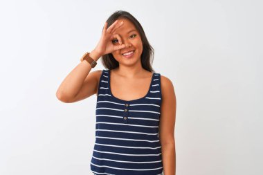 Çizgili tişört giyen genç Çinli kadın izole edilmiş beyaz arka planda duruyor. El hareketleriyle gülümsüyor, gözleriyle mutlu yüzle parmaklarının arasından bakıyor..