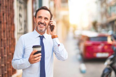 Orta yaşlı yakışıklı işadamı akıllı telefondan konuşuyor. İçiyor, kahveyi götürüyor, gülümsüyor.