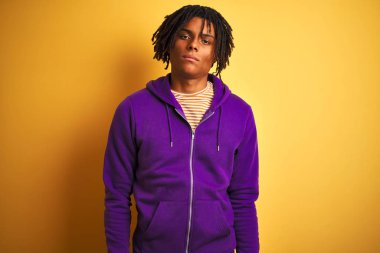 Siyah saçlı, mor eşofmanlı, izole edilmiş mor arka planı olan, yüzünde ciddi bir ifadeyle Afro-Amerikan bir adam. Basit ve doğal bir şekilde kameraya bakıyorsun..