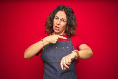 Kırmızı izole edilmiş arka planda önlük giyen orta yaşlı bir kadın. Aceleyle zamanı, sabırsızlığı, gecikmeyi izlemek için acele ediyor.