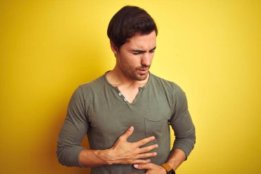 Genç, yakışıklı bir adam, mide bulantısı, acı verici bir hastalık yüzünden izole edilmiş sarı arka plan üzerinde dikiliyor. Ache kavramı.