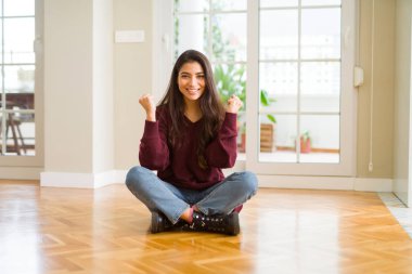 Evde katta oturan genç güzel kadın şaşırmış ve başarı için hayran kaldırdı Kollarını açarak kutluyor ve gözleri açık. Kazanan kavramı.