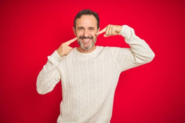 Yakışıklı orta yaşlı, gri saçlı, izole edilmiş kırmızı arka planı olan neşeli gülümseyen ve parmaklarıyla ve ağzıyla işaret eden yaşlı bir adam. Diş sağlığı konsepti.