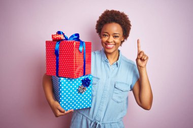 Doğumgünü hediyelerini pembe izole edilmiş arka planda tutan Afrikalı Amerikalı bir kadın bir fikir ya da soru işareti ile şaşırdı.