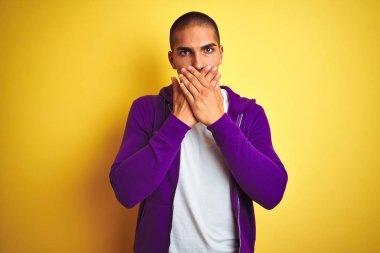 Sarı arka plan üzerine mor kazak giyen genç yakışıklı adam yanlışlıkla elleri ile ağzını kapatırken şok oldu. Gizli konsept.