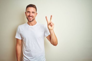 Yakışıklı delikanlı gösterilen ve parmakları ile işaret izole arka plan üzerinde rahat beyaz t-shirt giyen ikincisi ise kendinden emin ve mutlu gülümseyerek.