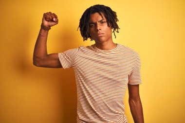 Sarı arka planda duran çizgili tişörtlü Afro adam güçlü, kendinden emin ve gururlu biri.