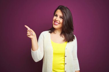 Genç, güzel, esmer bir kadın. Mor izole edilmiş arka planda bir ceket. Yüzünde kocaman bir gülümseme var..