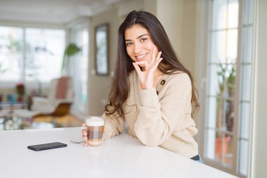 Evde kahve içen genç bir kadın parmaklarıyla imza atıyor, mükemmel bir sembol.