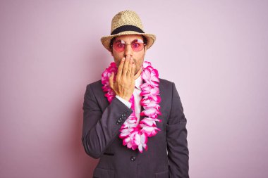 Takım elbiseli genç işadamı şapka gözlüğü takıyor, Hawaii lei pembe arka plan üzerini örtüyor. Ağzı, hata yüzünden utançla dolu, korkunun ifadesi, sessizlikten korkmak, gizli konsept.