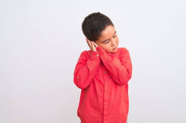 Zarif kırmızı gömlek giyen güzel bir çocuk izole edilmiş beyaz arka plan üzerinde duruyor yorgun uyuyor ve elleri ile birlikte poz verirken kapalı gözlerle gülümsüyor..