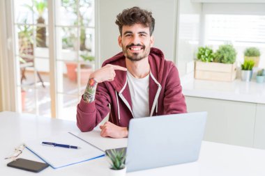Bilgisayar laptop ve defter sürpriz yüz işaret parmağı kendisine kullanan genç öğrenci adam