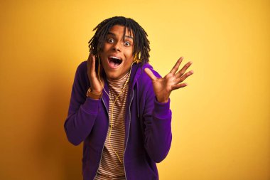 Rastalı Afro adam müzik dinliyor. Sarı arka planda kulaklık takıyor. Çok mutlu ve heyecanlı.