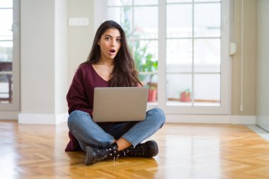 Bilgisayarda dizüstü bilgisayar kullanan genç bir kadın yerde korkmuş ve şok olmuş bir şekilde oturuyor..
