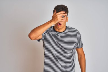 Genç Hintli adam, donanma çizgili tişört giyiyordu. İzole edilmiş beyaz arka planda duruyordu. Şok olmuş bir şekilde yüzünü ve gözlerini kapatıyordu..