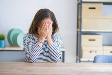 Orta yaş kıdemli kadın ağlarken elleri ile yüz kapsayan üzücü ifade ile evde masada oturuyor. Depresyon konsepti.