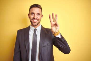 Sarı arkaplan üzerinde genç ve yakışıklı bir iş adamı üç numarayı gösterip işaret ederken kendinden emin ve mutlu bir şekilde gülümsüyor..