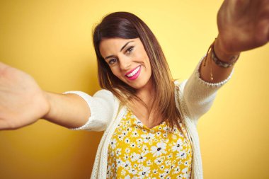 Sarı arka plan üzerinde duran ceketli güzel bir kadın kucaklanmak için kollarını açmış gülümseyen kameraya bakıyor. Mutluluğu kucaklayan neşeli bir ifade..