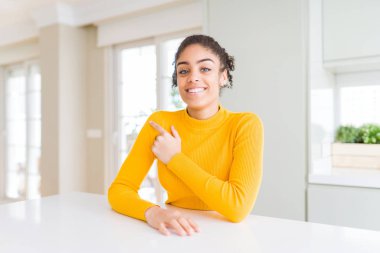 Afro saçlı güzel Afro-Amerikalı kadın günlük sarı bir süveter giyiyordu. Neşeli, yüzünde bir gülümseme vardı. Yüzünde mutlu ve doğal bir ifade vardı.