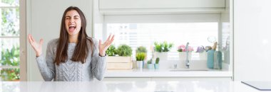 Evde beyaz masada oturan güzel genç kadının geniş açılı resmi deli ve deli bağırarak ve agresif ifade ve kollar kaldırdı ile bağırıyor. Hayal kırıklığı kavramı.