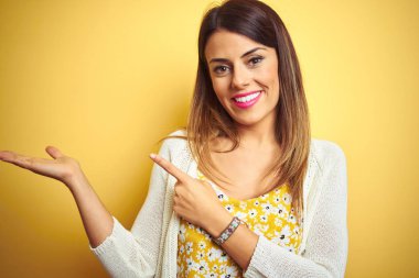 Sarı arka plan üzerinde duran ceketli genç ve güzel bir kadın hayrete düşmüş ve kameraya gülümsüyor..