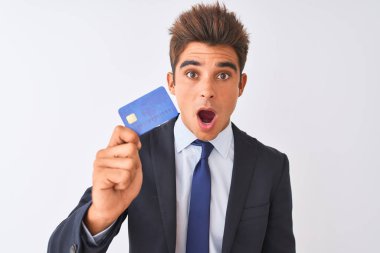 Soyutlanmış beyaz arka planda kredi kartı tutan takım elbiseli genç ve yakışıklı bir işadamı. Şaşırmış bir yüzle korkmuş ve korku ifadesinden heyecanlanmış.