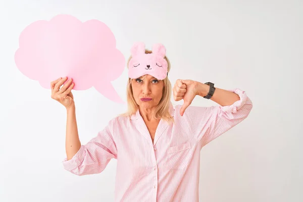 Middle age woman wearing sleep mask holding speech bubble over isolated white background with angry face, negative sign showing dislike with thumbs down, rejection concept