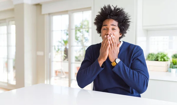 Young african american man wearing casual sweater sitting at home laughing and embarrassed giggle covering mouth with hands, gossip and scandal concept