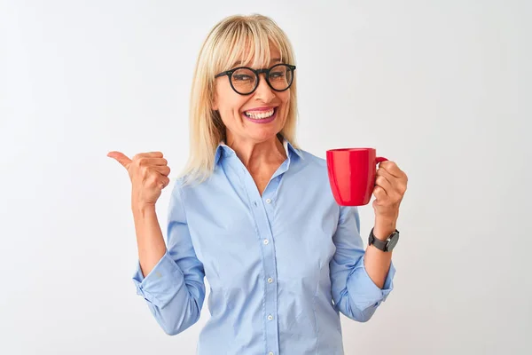 Middle age businesswoman wearing glasses drinking coffee over isolated white background pointing and showing with thumb up to the side with happy face smiling