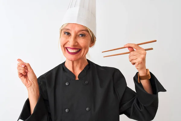 中年厨师女人头戴帽子 拿着筷子 站在孤立的白色背景上 很高兴手指手画脚地指向旁边 — 图库照片