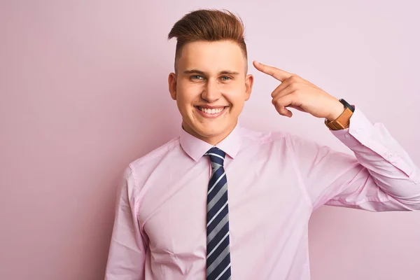 年轻英俊的生意人 身穿衬衫 打着领带 站在孤立的粉色背景上 微笑着 用一个手指指着头 很好的主意或想法 好的记忆力 — 图库照片