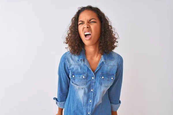 stock image Young brazilian woman wearing denim shirt standing over isolated white background angry and mad screaming frustrated and furious, shouting with anger. Rage and aggressive concept.