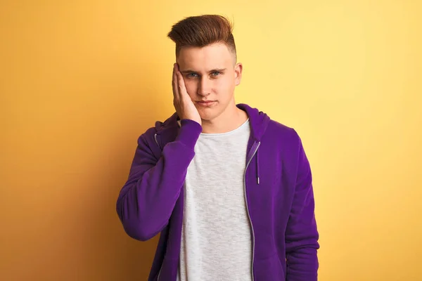 年轻英俊的男人穿着紫色的运动衫 站在孤立的黄色背景上 满脑子疲惫 两臂交叉的抑郁症使他厌烦 — 图库照片