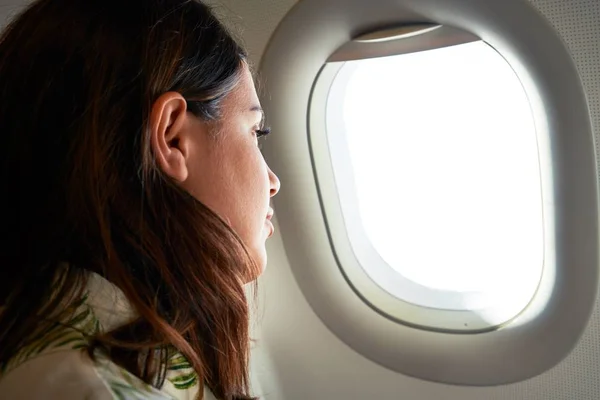 Young traveller woman sitting inside plane at the airport with sky view from the window