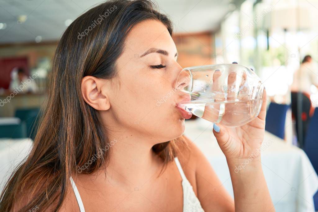 Young beautiful woman sitting at restaurant enjoying summer vacation drinking glass of water