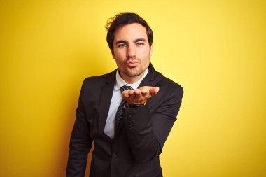 Takım elbiseli ve kravatlı genç yakışıklı bir işadamı izole edilmiş sarı arka planda dikilip havada öpüşürken kameraya bakıyor. Güzel ve seksi. Aşk ifadesi.