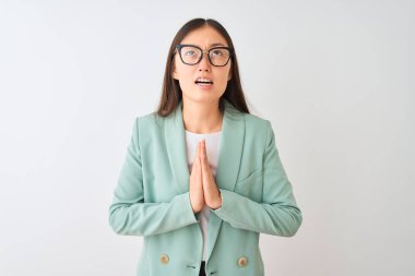 Zarif bir ceket ve gözlük takan Çinli iş kadını, izole edilmiş beyaz arka plan üzerinde yalvarıyor ve dua ediyor. Yüzünde umut ifadesi olan çok duygusal ve endişeli bir ifade var. Af diliyor. Din kavramı.