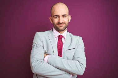 Mor izole edilmiş arka plan üzerinde takım elbise ve kravat giyen genç iş adamı kameraya bakarken kollarını kavuşturup gülümsüyor. Pozitif kişi.