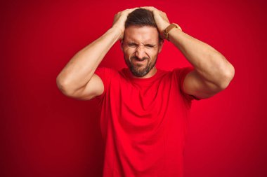 Kırmızı arka plan üzerine günlük tişört giyen genç yakışıklı adam acı ve migren yüzünden çaresiz ve stresli bir baş ağrısından muzdarip. Ellerini başının üstüne koy..