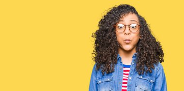 Genç güzel kadın kıvırcık saçlı gözlüklü komik surat ile yanakları şişirme. Ağız ile hava, deli ifade şişirilmiş.