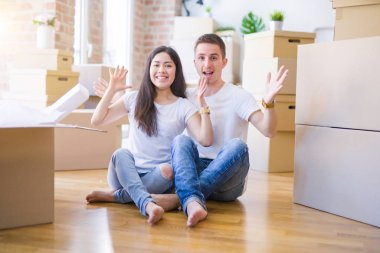 Genç ve güzel bir çift, yeni evlerinde karton kutuların etrafında oturmuş mutlu ve heyecanlı bir şekilde zaferi kutluyorlar.