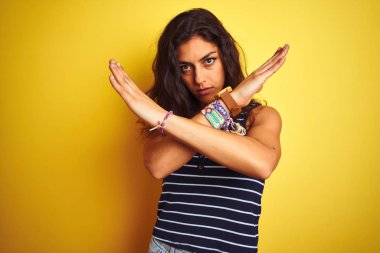 İzole edilmiş sarı arka plan üzerinde duran çizgili tişört giyen genç ve güzel bir kadın. Reddedilmiş yüz ifadesi.