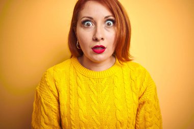 Kışlık süveter giyen genç bir kadın izole edilmiş sarı arka planda duruyor. Şaşırmış ve korkmuş bir ifade, korku ve heyecanlı bir yüz ifadesi var..