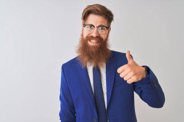 Genç, kızıl saçlı, takım elbiseli ve gözlüklü bir iş adamı izole edilmiş beyaz arka planda mutlu bir el hareketi yapıyor. Kameraya bakıp başarıyı gösteren ifade onaylanıyor.