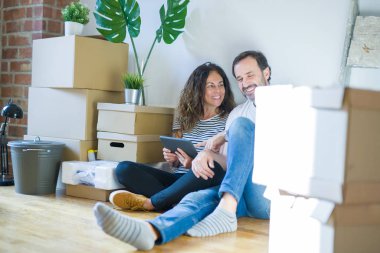 Orta yaş üst düzey romantik çift etrafında karton kutular ile daire katında oturan ve yeni bir eve taşınmak için mutlu gülümseyen aşk