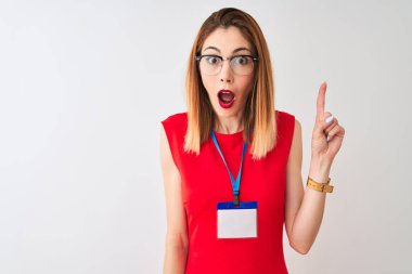 Konferanstaki kızıl saçlı iş kadını, izole edilmiş beyaz arka plan üzerinde kimlik kartıyla başarılı bir fikri işaret ediyor. Heyecanlı ve mutlu. Bir numara..