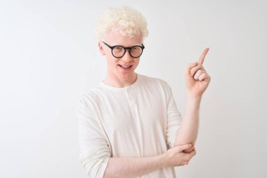 Genç albino tişört ve gözlüklü adam izole edilmiş beyaz arka planda duruyor. Yüzünde kocaman bir gülümseme var. Eli ve parmağı kameraya bakıyor..