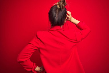 Genç ve güzel bir iş kadını kırmızı izole edilmiş arka planda dikiliyor. Elleri başının üstünde şüpheyi düşünüyor.