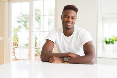 Beyaz masadaki yakışıklı Afro-Amerikalı adam kameraya seksi bir ifadeyle bakıyor, neşeli ve mutlu bir yüzle..